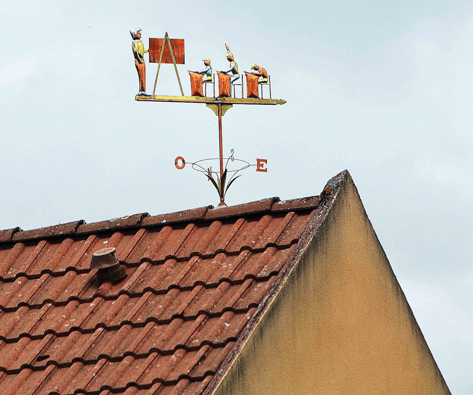 Girouette ornementale rouillée sur toit de tuiles avec figurines de travailleurs et points cardinaux O et E